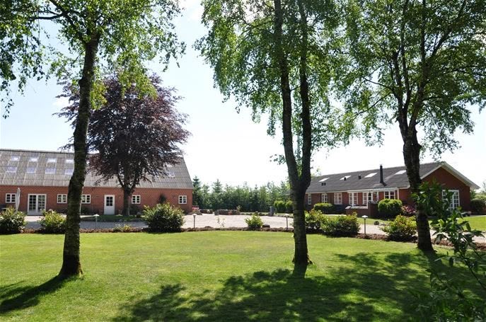 Rød murstensgård med grøn have og træer