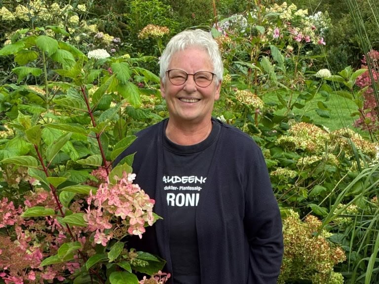 Smilende person står i blomstrende have