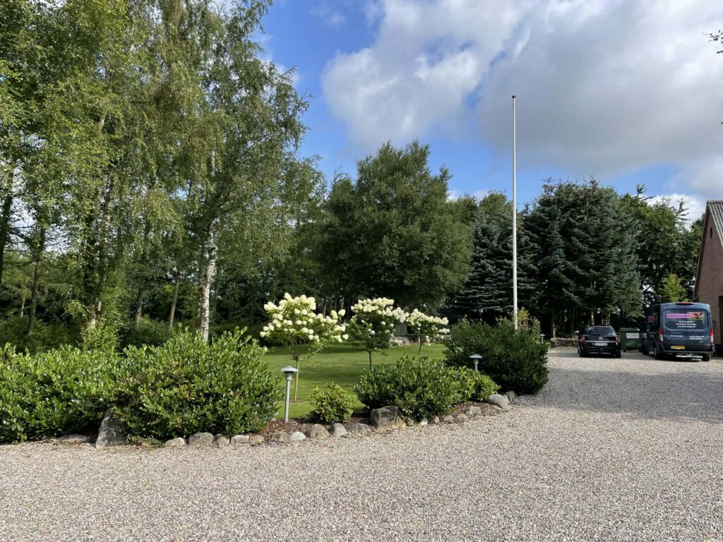 Grusindkørsel foran hus med have og træer