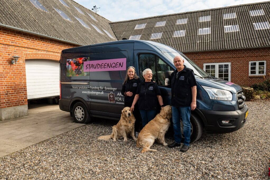 Tre personer og to hunde foran firmabil